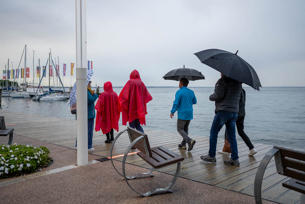 Touristen laufen mit Regenschirmen an der Seepromenade von Bardolino