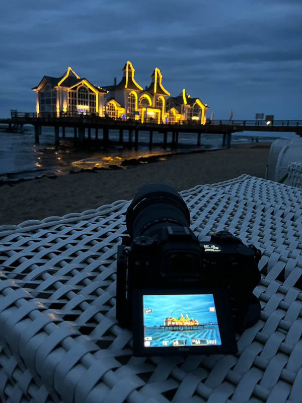 Die Kamera liegt auf einem Strandkorb um davon die Seebrücke zu fotografieren